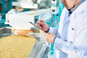 Mid section portrait of unrecognizable factory worker doing production quality inspection in food industry holding clipboard and standing by conveyor belt